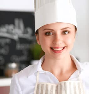 Smiling female chef in white uniform and striped apron in a modern kitchen, representing air fryer recipe blogger Riley Morgan.