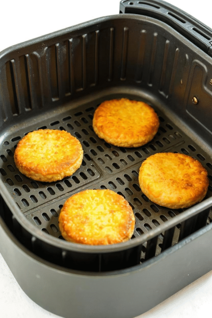 Four golden chicken patties cooking in an air fryer basket