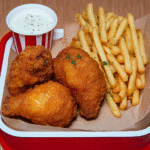 A red tray with crispy fried chicken drumsticks and a box of golden French fries.