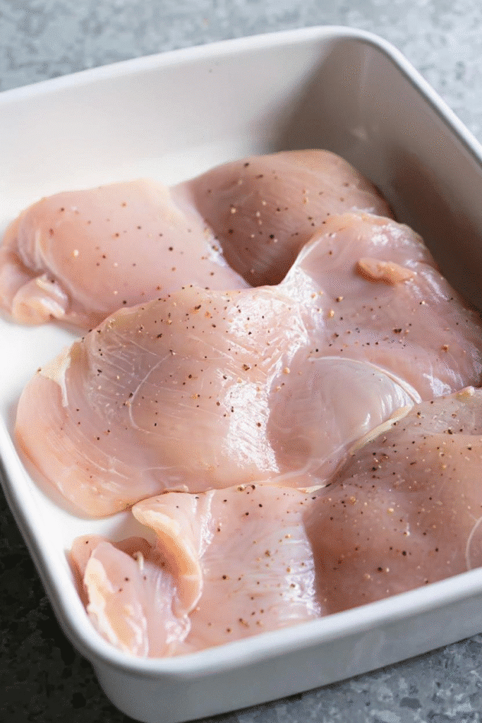 Raw chicken thighs seasoned with salt and pepper in a white dish