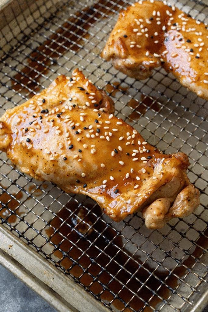 Cooked teriyaki chicken thighs in air fryer tray topped with sesame seeds